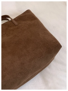 Detail of soft brown plush tote bag texture with leather handle and precision stitching