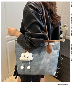 Detail of blue denim tote bag with leather straps and cute white cloud plush pendant