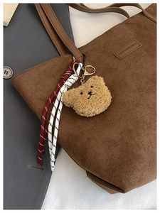 Detail of cute plush bear charm with gold metal hook on a brown canvas tote bag