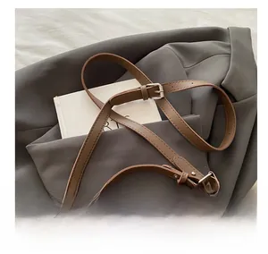 Detail of dark brown woven shoulder bag with adjustable leather strap on gray blazer