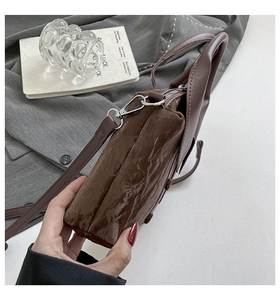Détail du sac en similicuir marron foncé plissé montrant la texture brillante et l'argent