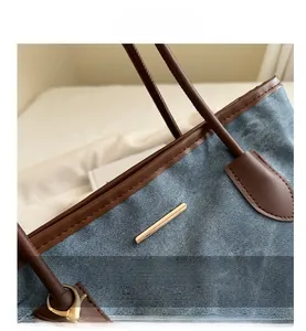 Detail of blue denim tote bag with brown leather trim and polished gold metal hardware