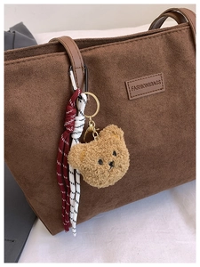 Detail of a brown fuzzy bear plush keychain with red rope on a dark suede tote bag