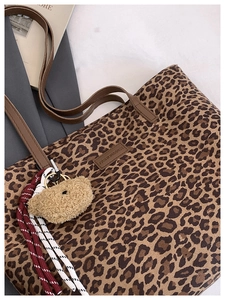 Detail of leopard print tote with brown leather logo tag and heart plush keychain