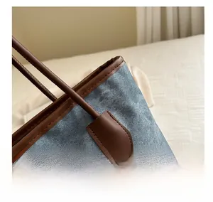 Detail of blue denim tote bag with brown leather trim and silver metal zipper puller