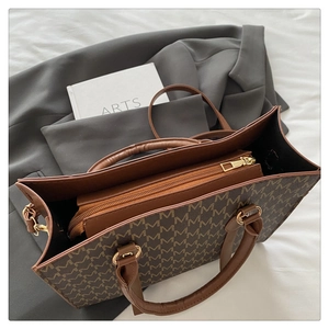 Close-up of brown tote bag with M-pattern logo and golden metal zipper detail