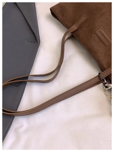 Detail of brown suede tote bag featuring a leather label and long shoulder straps