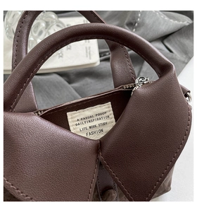 Détail d'un sac à main marron foncé en cuir grainé montrant le rabat design unique