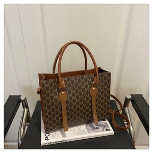 Classic large brown tote bag with M-pattern and shoulder strap on a magazine seat