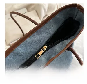 Detail of smooth gold-tone zipper closure and brown leather trim on denim tote bag