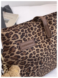 Detail of leopard print tote bag with brown leather handles and plush bear charm decoration