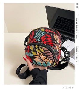 Detail of waterproof nylon crossbody bag featuring colorful leaf prints and dual zippers