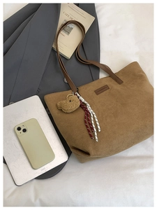 Close-up of brown corduroy tote bag with plush bear charm and leather strap on white linen