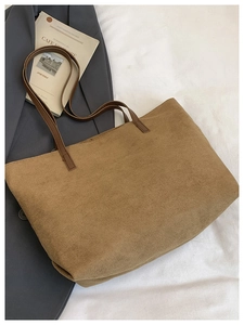 Detail of a large brown tote bag with premium matte texture and leather handles on soft white fabric