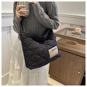 Close-up of black quilted tote bag featuring large diamond stitching and a fashion logo label
