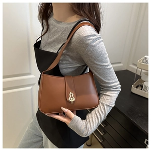 Detail of a warm brown crescent shoulder bag with a gold flame-shaped metal buckle