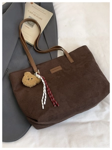 Close-up of brown corduroy tote bag featuring leather label and plush bear charm detail