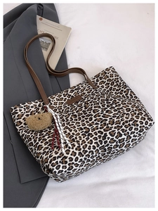 Detail of leopard print tote bag with brown leather straps and cute plush bear charm