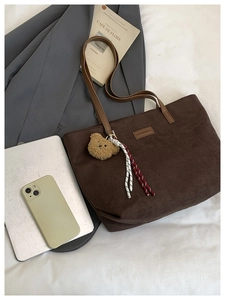 Flat lay of brown corduroy tote bag with plush bear charm and work essentials on desk