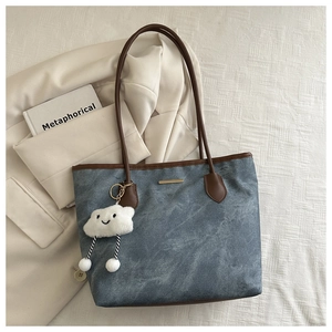 Détail d'un cabas en denim bleu avec anses en cuir marron et pendentif nuage