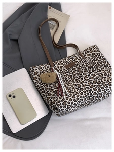 Close-up of leopard print tote bag with brown leather handles and plush bear charm decoration