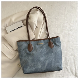 Détail du sac cabas à texture marbrée avec lanières brunes et boucle dorée sur tissu blanc