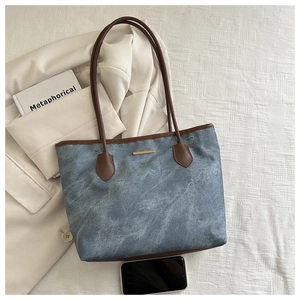 Détail du sac fourre-tout en denim bleu avec lanières en cuir marron et décor métallique