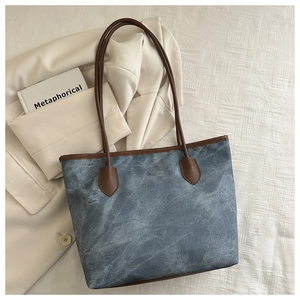 Détail du sac cabas bleu texturé avec anses en cuir marron et livre décoratif en arrière-plan