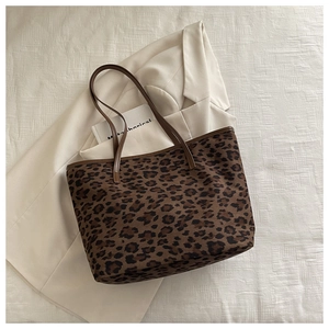 Detailed view of leopard print tote bag with brown leather straps on a beige blazer
