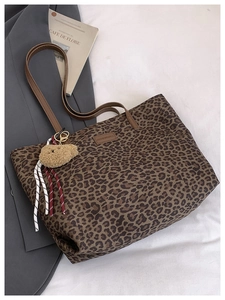 Detail of leopard print tote bag featuring brown faux leather handles and a plush bear charm