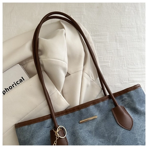 Vue détaillée du cabas en denim bleu avec anses en cuir marron et détails en métal doré