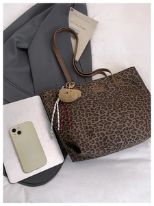 Close-up of leopard print tote bag with plush bear charm on white fabric background