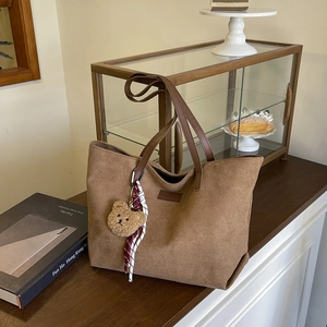 Brown matte tote bag with leather handles and plush bear charm in a cafe setting