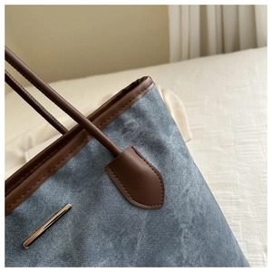Détail du tissu texturé bleu avec bordure en cuir marron et garniture dorée sur le cabas