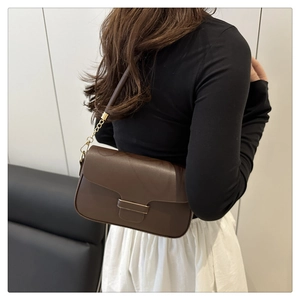 Detail of dark brown leather underarm bag with gold chain strap worn by a model
