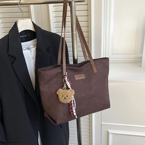 Deep brown suede tote bag with leather straps and teddy bear pendant hanging by a suit