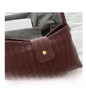 Close-up of wine red woven leather tote bag featuring a round golden metallic buckle