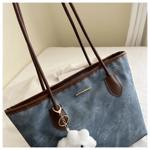 Détail d'un sac cabas en denim bleu avec bordures en cuir brun et breloque en peluche