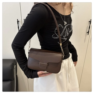 Détail d'un sac bandoulière marron foncé avec rabat incurvé et boucle métallique dorée