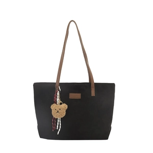 Minimalist black tote bag with brown straps and cute teddy bear charm on white background