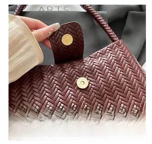 Detail shot of the golden magnetic buckle closure on a woven burgundy shoulder bag