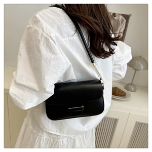 Détail d'un sac bandoulière noir en cuir avec boucle dorée porté sur une chemise blanche
