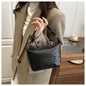 Detail of black woven leather shoulder bag styled on a beige wool coat for a chic look