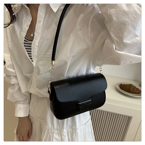 Lifestyle shot of black minimalist crossbody bag with gold chain strap worn on person