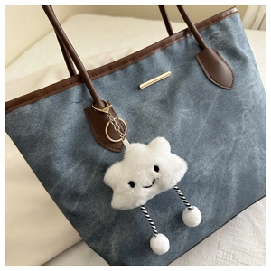 Détail d'un sac cabas en denim bleu avec lanières en cuir marron et un charme nuage blanc