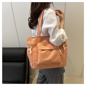 Side view of large orange-pink canvas tote bag on a model showing side pockets and straps