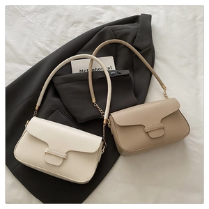 Flat lay of cream and tan minimalist shoulder bags with leather chain straps on suit