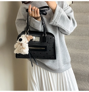 Detail of black polka dot shoulder bag with cute white plush dog charm on a strap