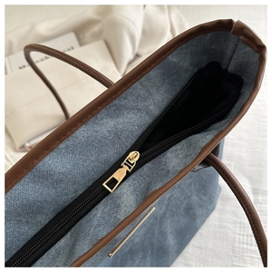 Détail de la fermeture éclair dorée sur le sac cabas en denim bleu et cuir marron