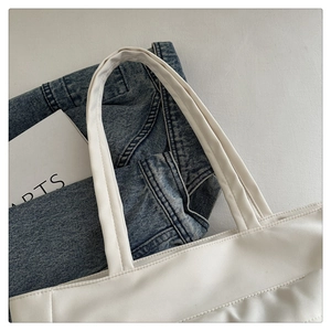 Detail view of white minimalist tote bag with neat stitching and artsy denim background